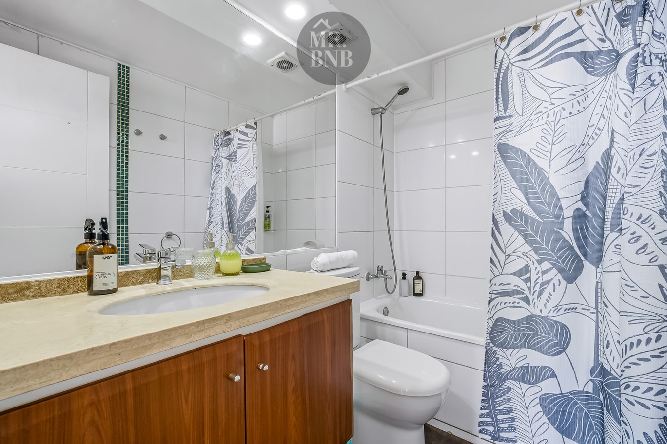 Baño con tina, ducha con cortina, lavamanos y amenities sobre la encimera.