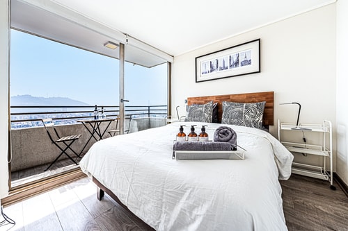 Dormitorio con cama, ventanal con vista panorámica y acceso a balcón