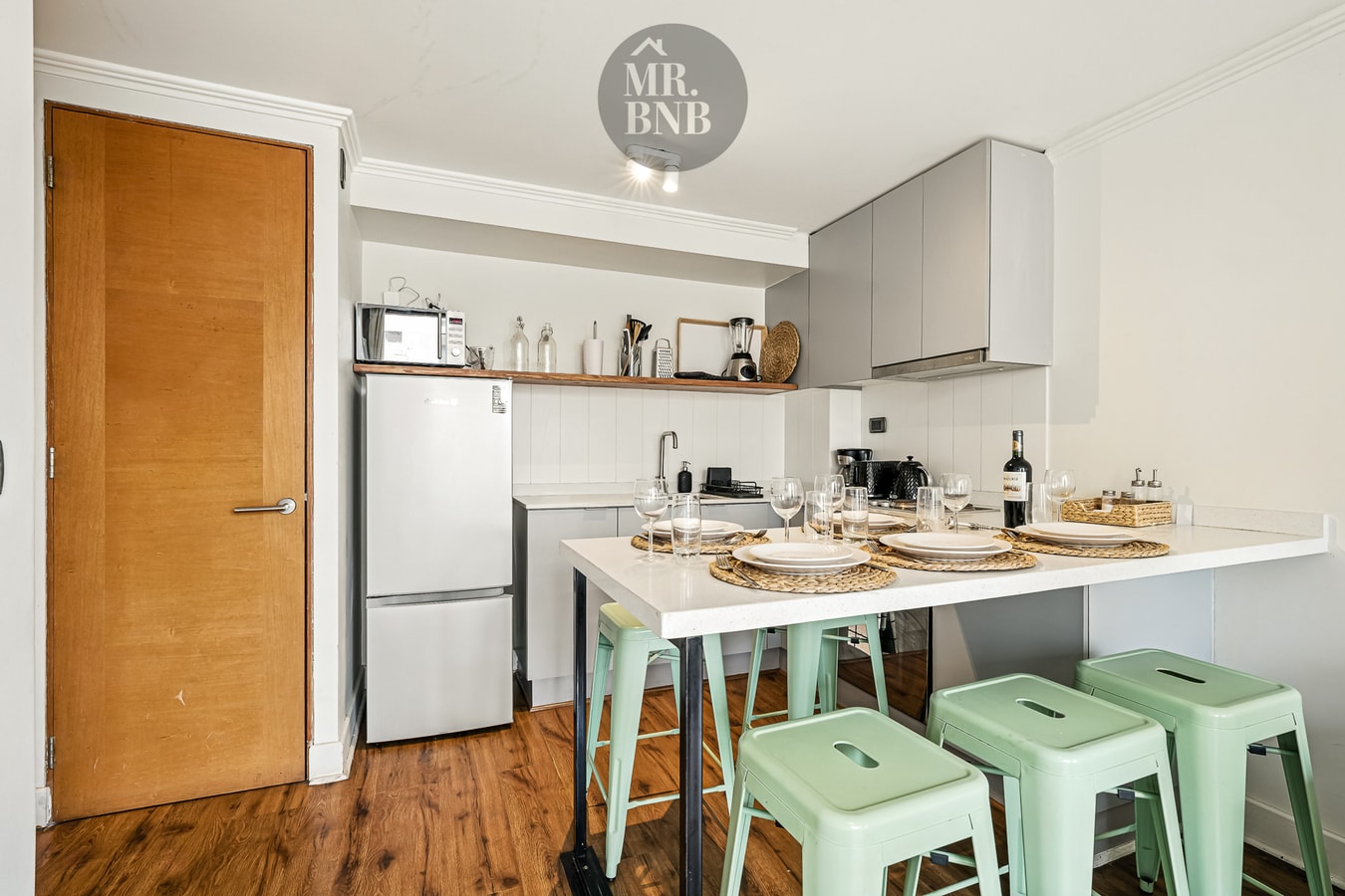 Cocina con puerta de acceso, refrigerador, muebles altos y barra con taburetes verdes