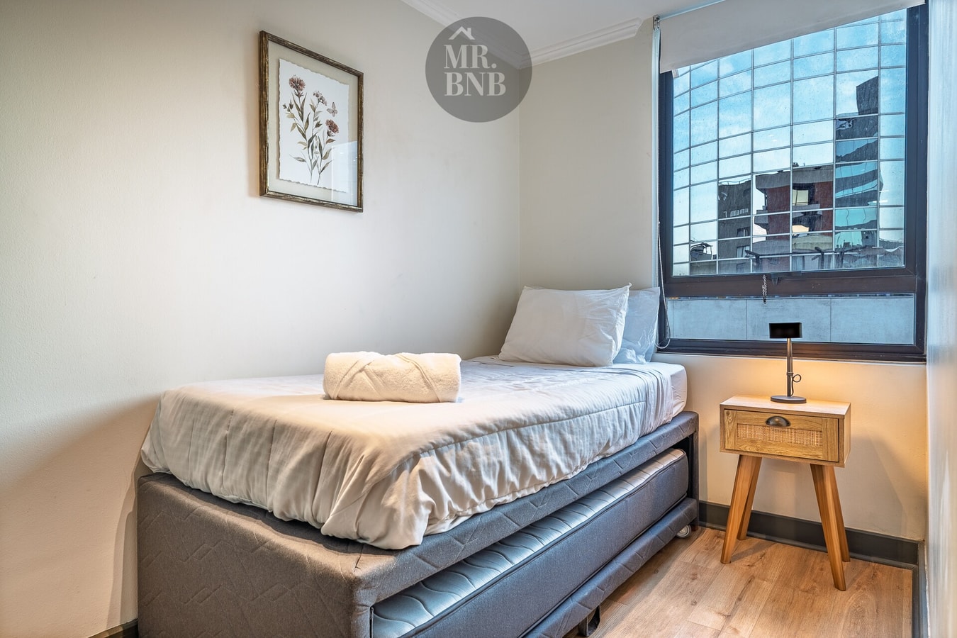 Dormitorio con cama individual, velador de madera y piso flotante