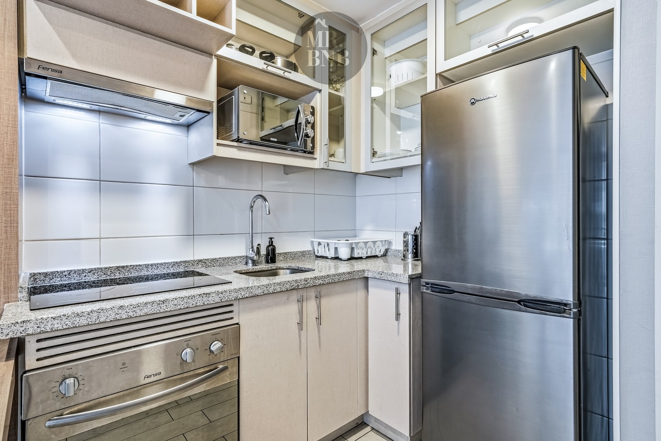 Cocina con refrigerador, horno, encimera y muebles claros
