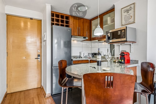 Comedor con mesa y sillas de cuero junto a la puerta de acceso, cocina al fondo.