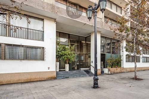 Fachada y acceso del edificio, con reja de acceso y árboles en la vereda