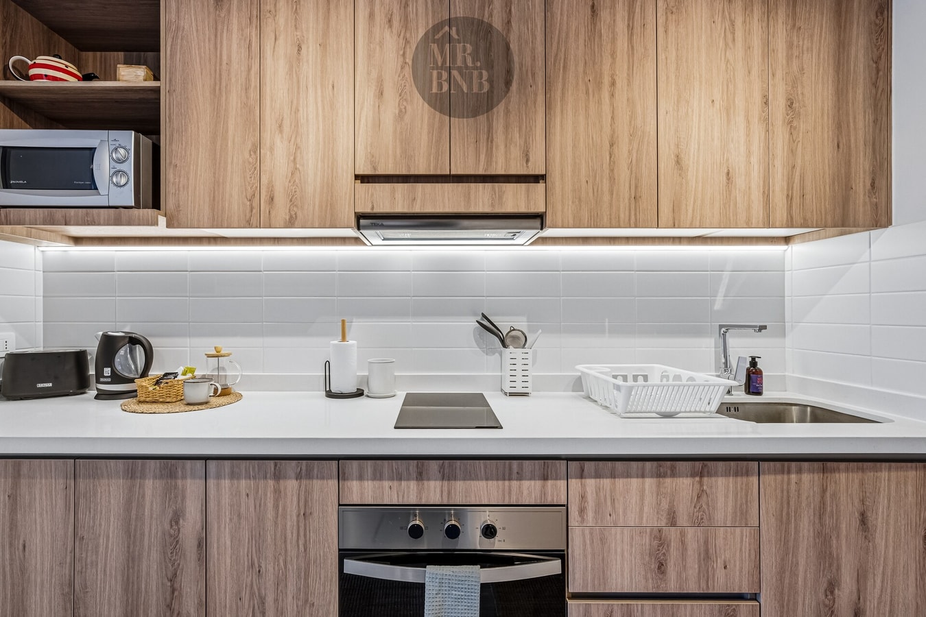 Detalle de cocina con muebles de madera, encimera blanca y cocina eléctrica