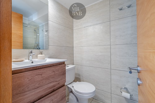 Baño con mueble de madera, lavamanos, inodoro y espejo
