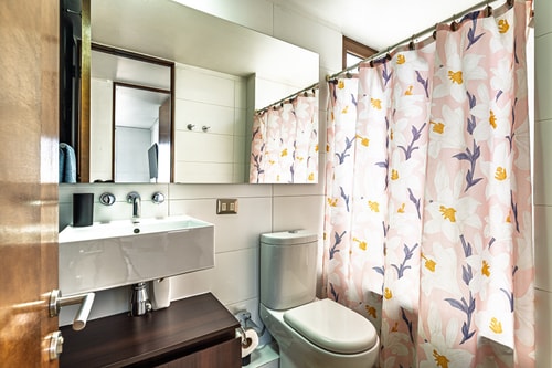Baño con cortina floral, lavamanos y toallero de madera