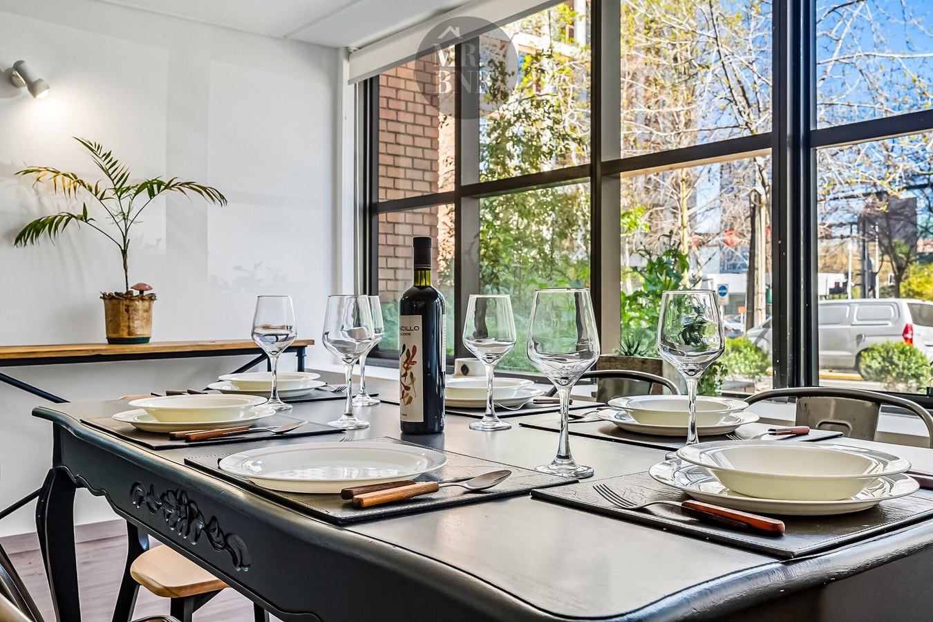 Comedor junto a ventanales amplios con vista a la calle, copas y botella sobre la mesa