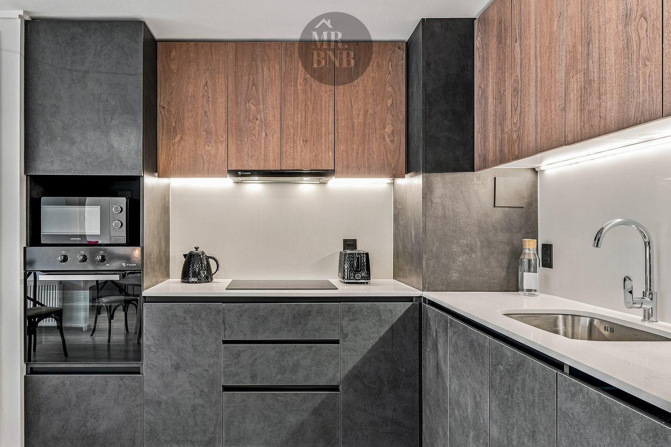 Cocina equipada con muebles en madera y negro, encimera y campana extractora.