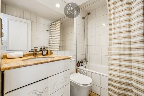 Baño con tina, cortina a rayas, lavamanos con cubierta de mármol y toallas dispuestas junto al espejo