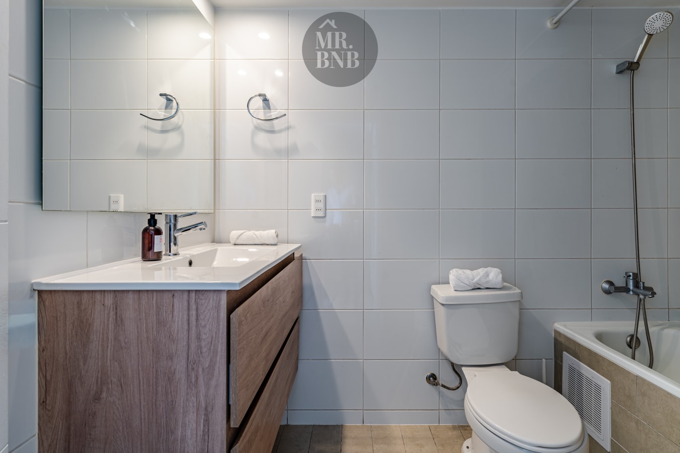 Baño con doble llave de ducha, mueble vanitorio de madera, inodoro y tina