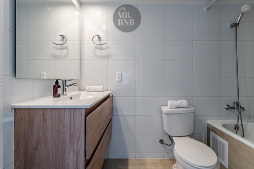 Baño con doble llave de ducha, mueble vanitorio de madera, inodoro y tina