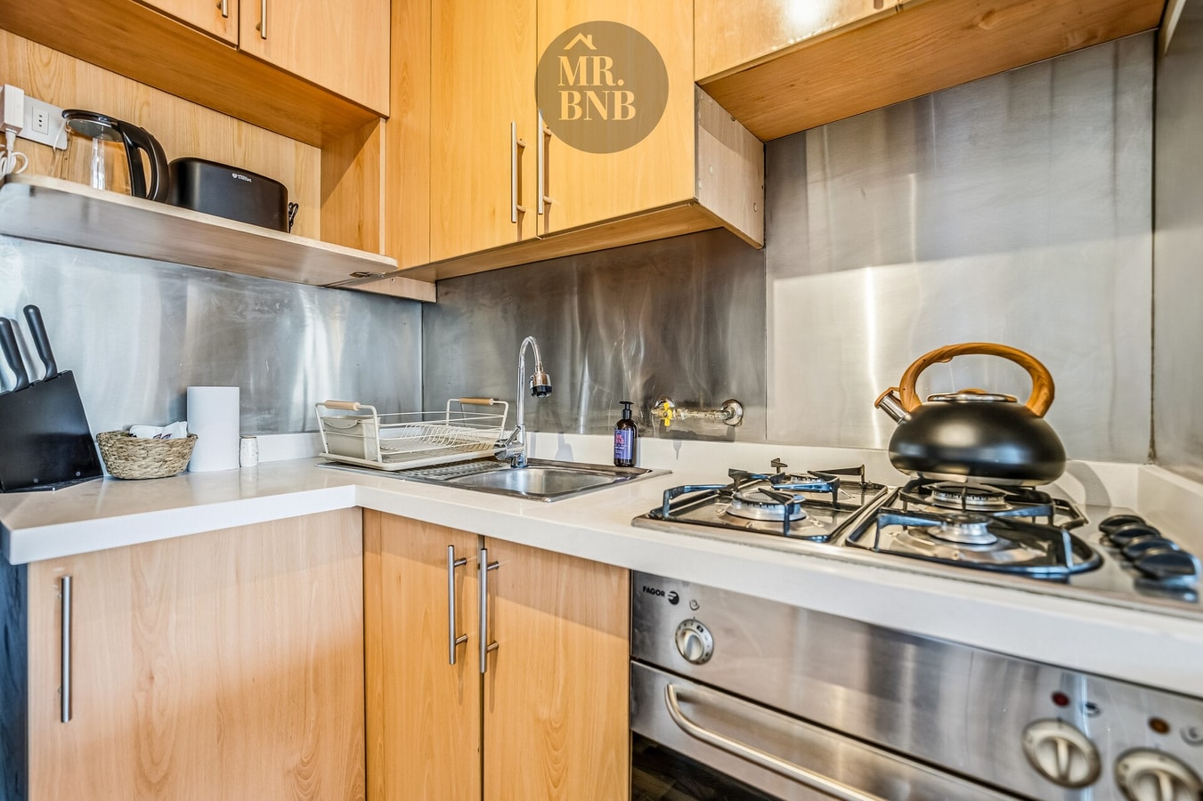 Cocina de madera con cocina a gas, hervidor y muebles altos.
