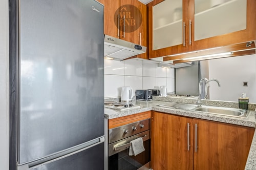 Refrigerador y muebles de cocina en madera, con extractor y utensilios sobre la encimera.