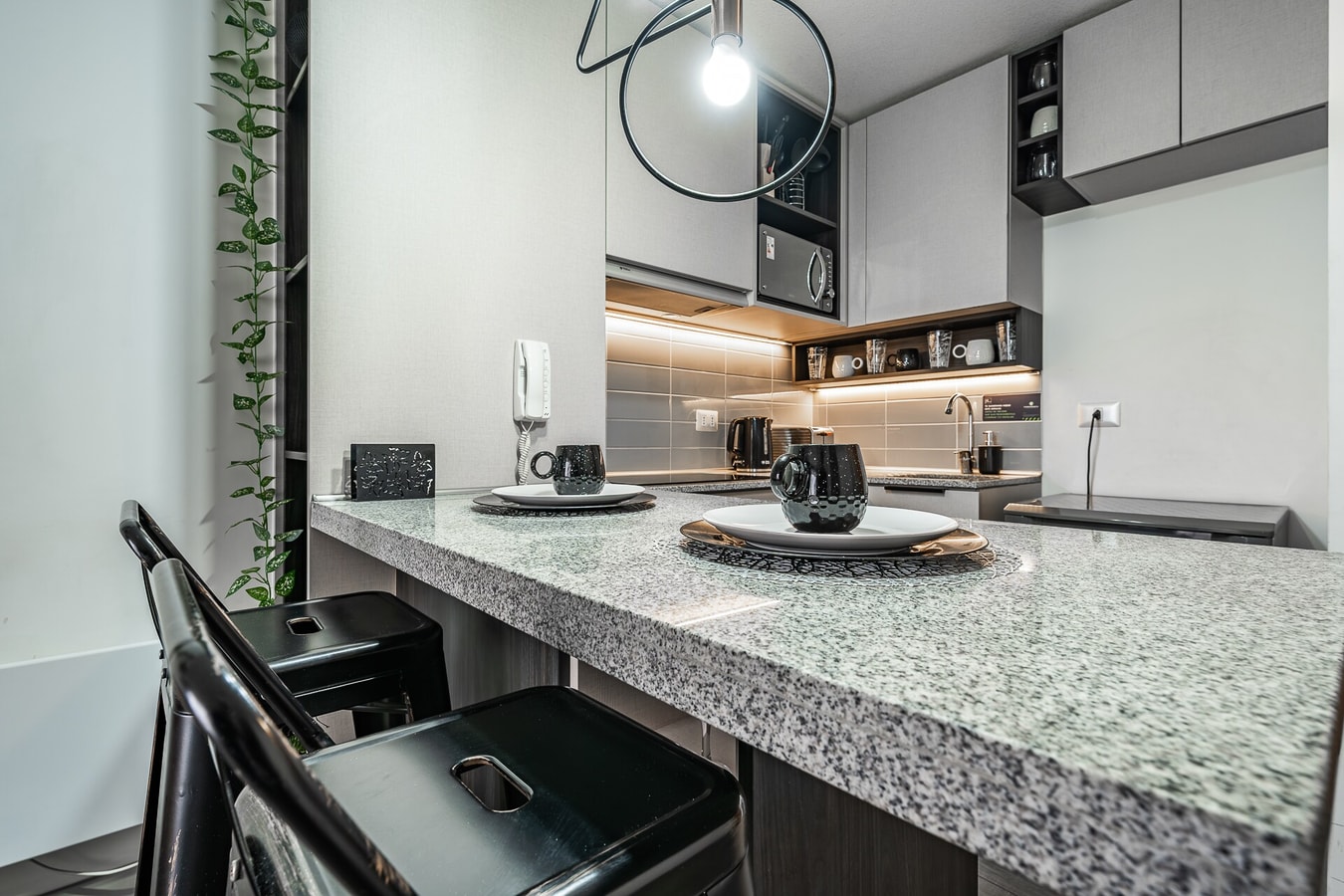 Detalle de la barra de cocina en piedra con banqueta y estantería iluminada al fondo