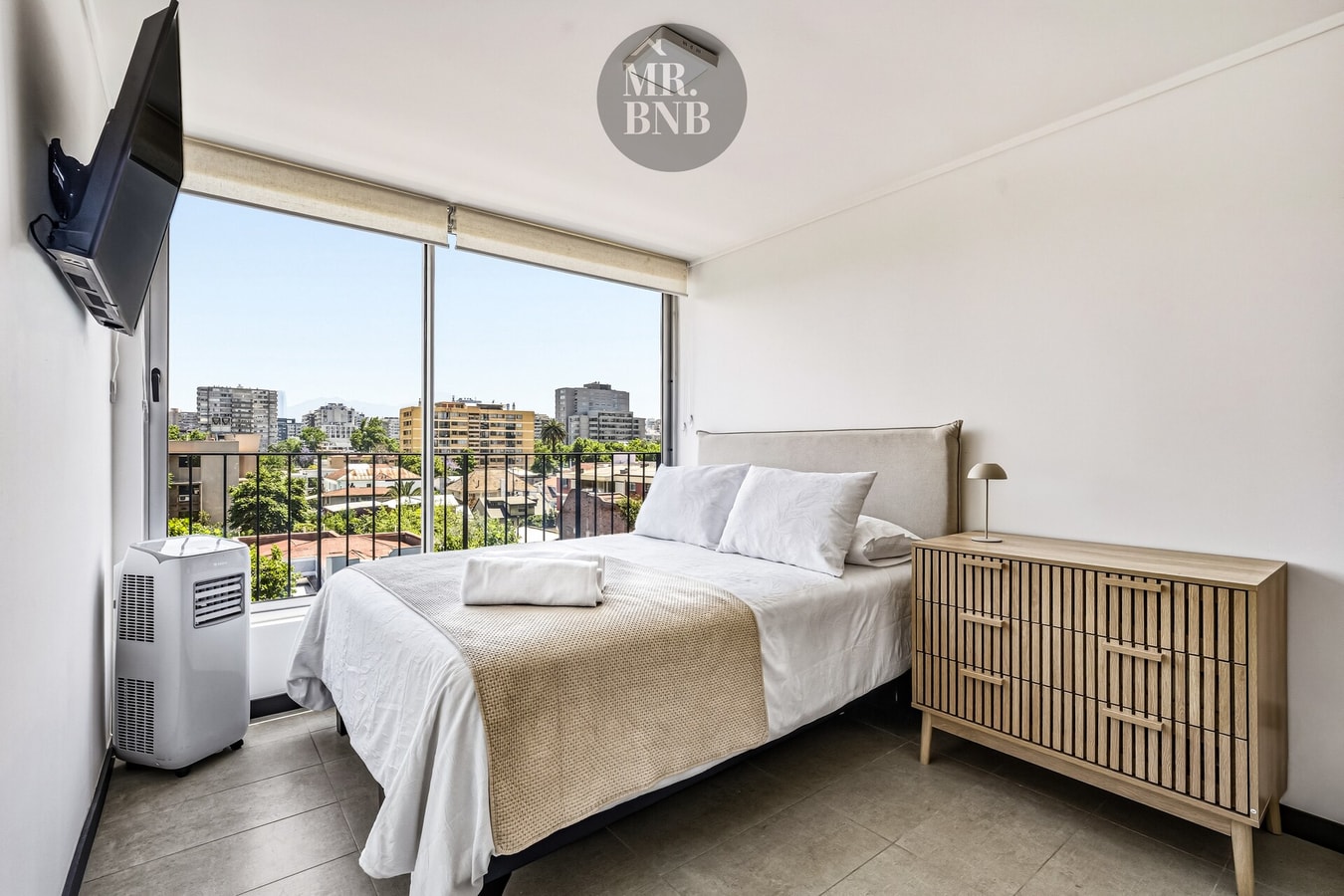 Dormitorio con cama, televisor en la pared y ventanal con vista a la ciudad