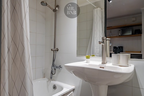 Baño con ducha, tina, lavamanos pedestal y repisas con amenities