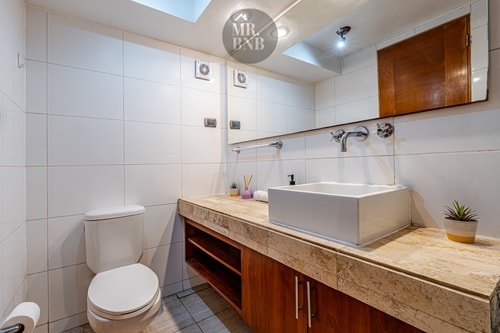 Baño con lavamanos sobre mueble de madera, inodoro y espejo grande