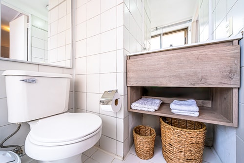 Baño con inodoro, repisa de madera con toallas y canastos
