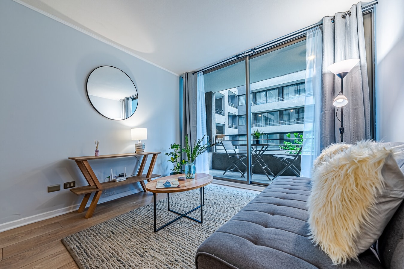Living con sofá gris, espejo redondo y ventana hacia el balcón