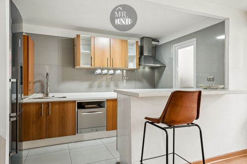 Cocina en L con isla, banqueta de cuero y muebles de madera
