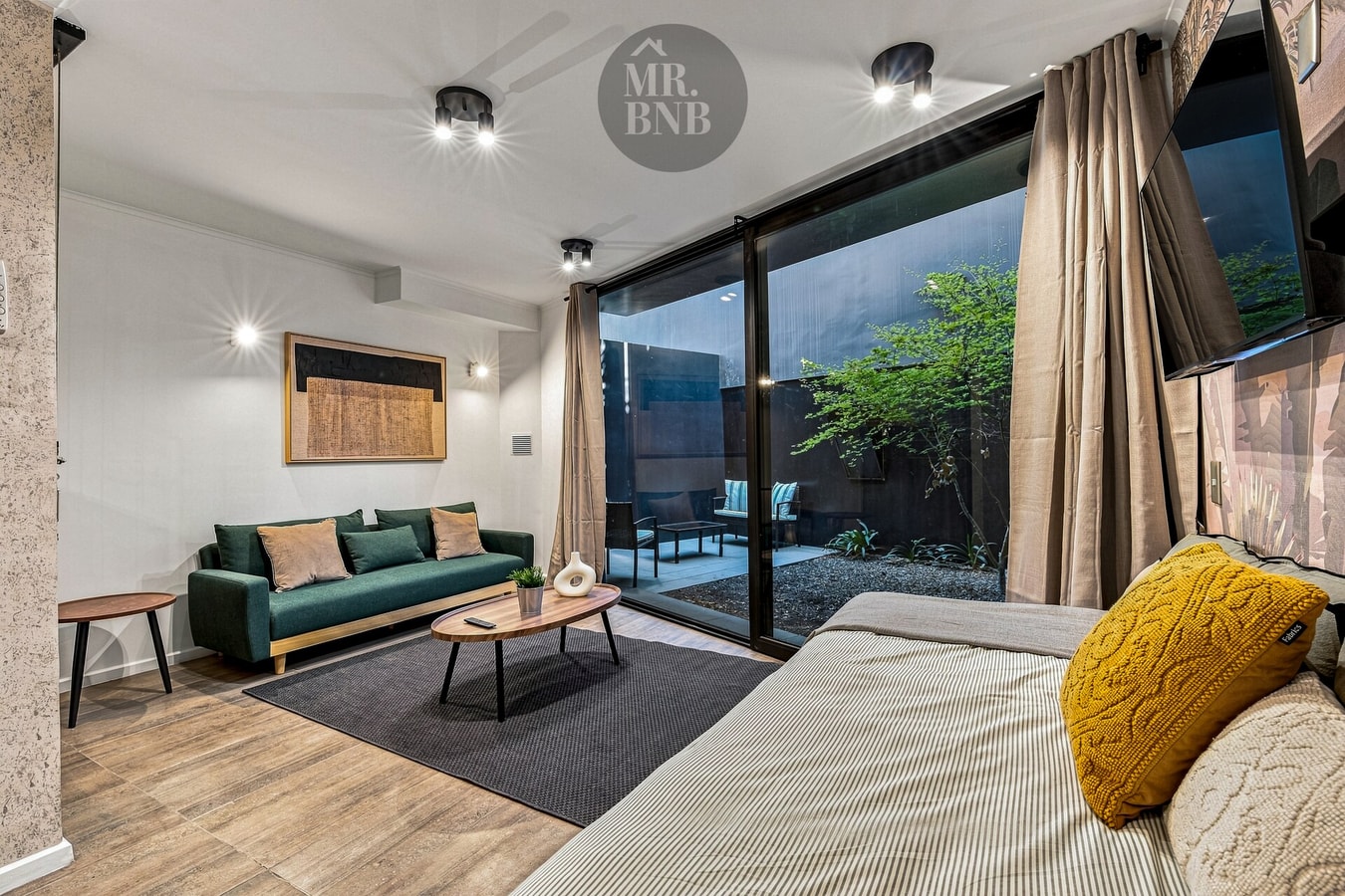 Living con sofá verde y puf amarillo, mesa de centro, ventanal corredizo hacia el patio y TV