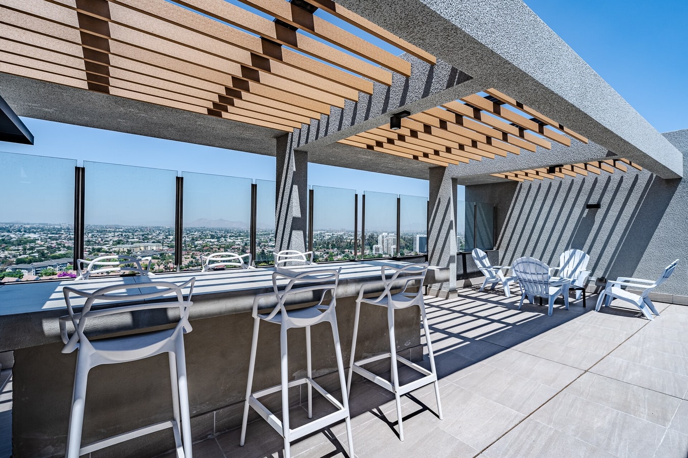Terraza en altura con pérgola de madera, barra con banquetas y vista panorámica de la ciudad.