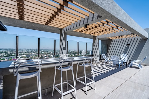 Terraza en altura con pérgola de madera, barra con banquetas y vista panorámica de la ciudad.