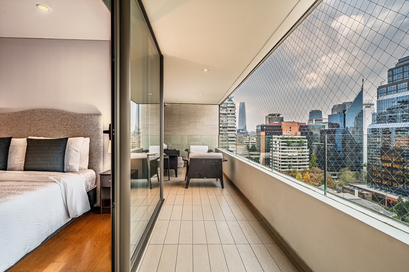 Dormitorio con cama y balcón con vista a la ciudad y sector de estar.