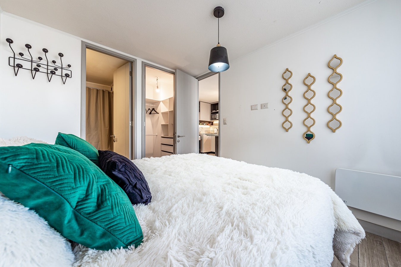 Dormitorio con cama de dos plazas, cojines verdes y azules, colgador de pared y closet al fondo