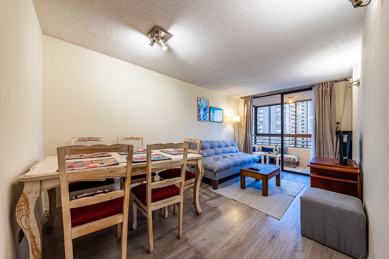 Living comedor con mesa de madera para seis personas, sofá azul y piso flotante.