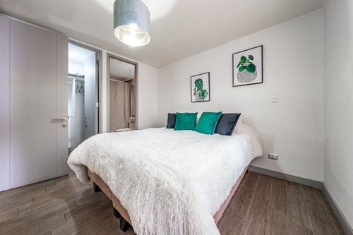 Dormitorio con cama con textil blanco, cojines verdes y dos cuadros decorativos sobre el respaldo