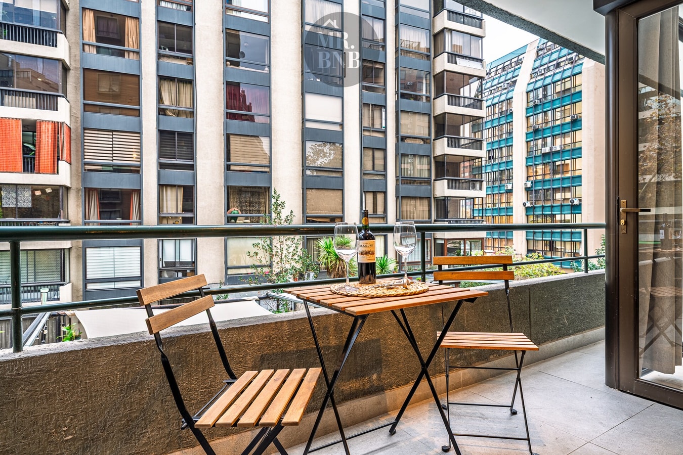 Terraza del departamento con mesa y dos sillas plegables, vista a edificios vecinos