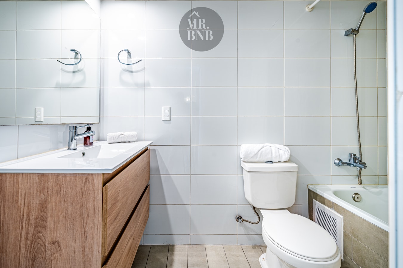 Baño con doble llave de lavamanos, tina con ducha e inodoro.