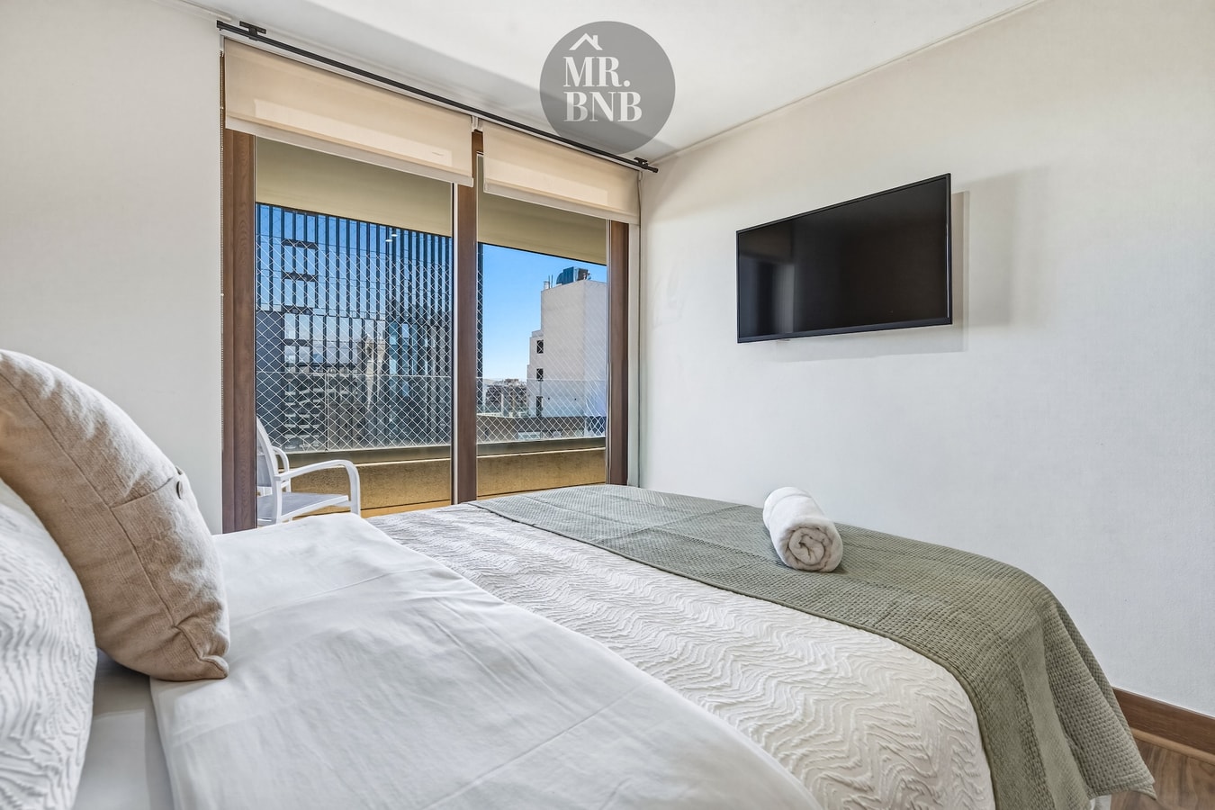 Dormitorio con dos camas, televisor en la pared y ventana hacia el exterior.