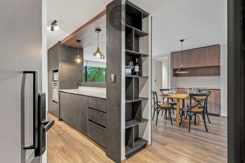 Cocina equipada con isla y estantería abierta, con vista hacia el comedor de madera oscura