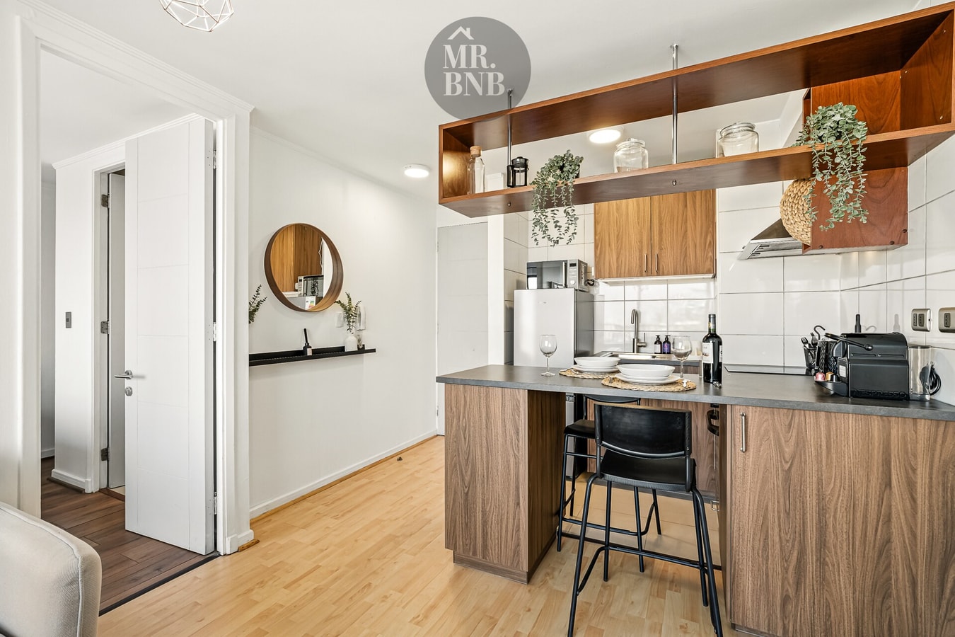 Cocina abierta en madera con barra alta, banquetas y estantería con plantas