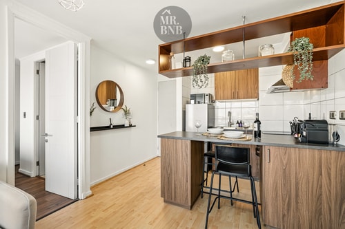 Cocina abierta en madera con barra alta, banquetas y estantería con plantas