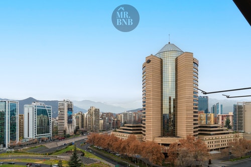Vista panorámica de la ciudad y la cordillera de los Andes desde la altura, con una torre emblemática al centro.