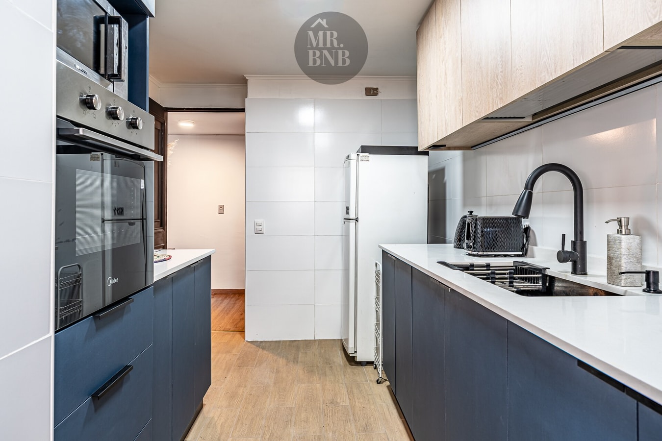 Cocina en ángulo más amplio, horno y microondas empotrados, refrigerador blanco