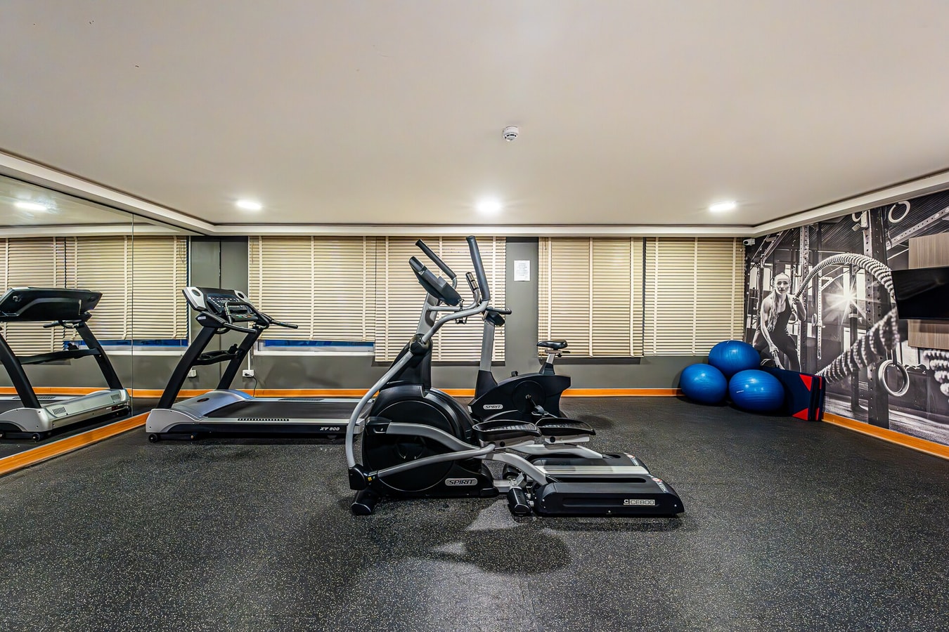 Gimnasio del edificio con trotadoras, elíptica, balones de pilates y mural deportivo en la pared