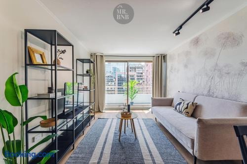 Living con sofá, repisa metálica con plantas y ventanal hacia el balcón.