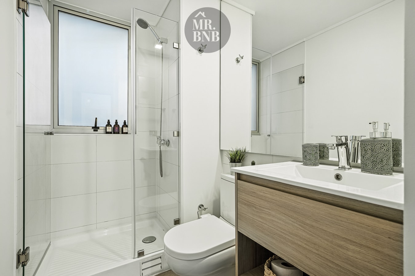 Baño con ducha de vidrio, inodoro y mueble de vanitorio en madera clara.