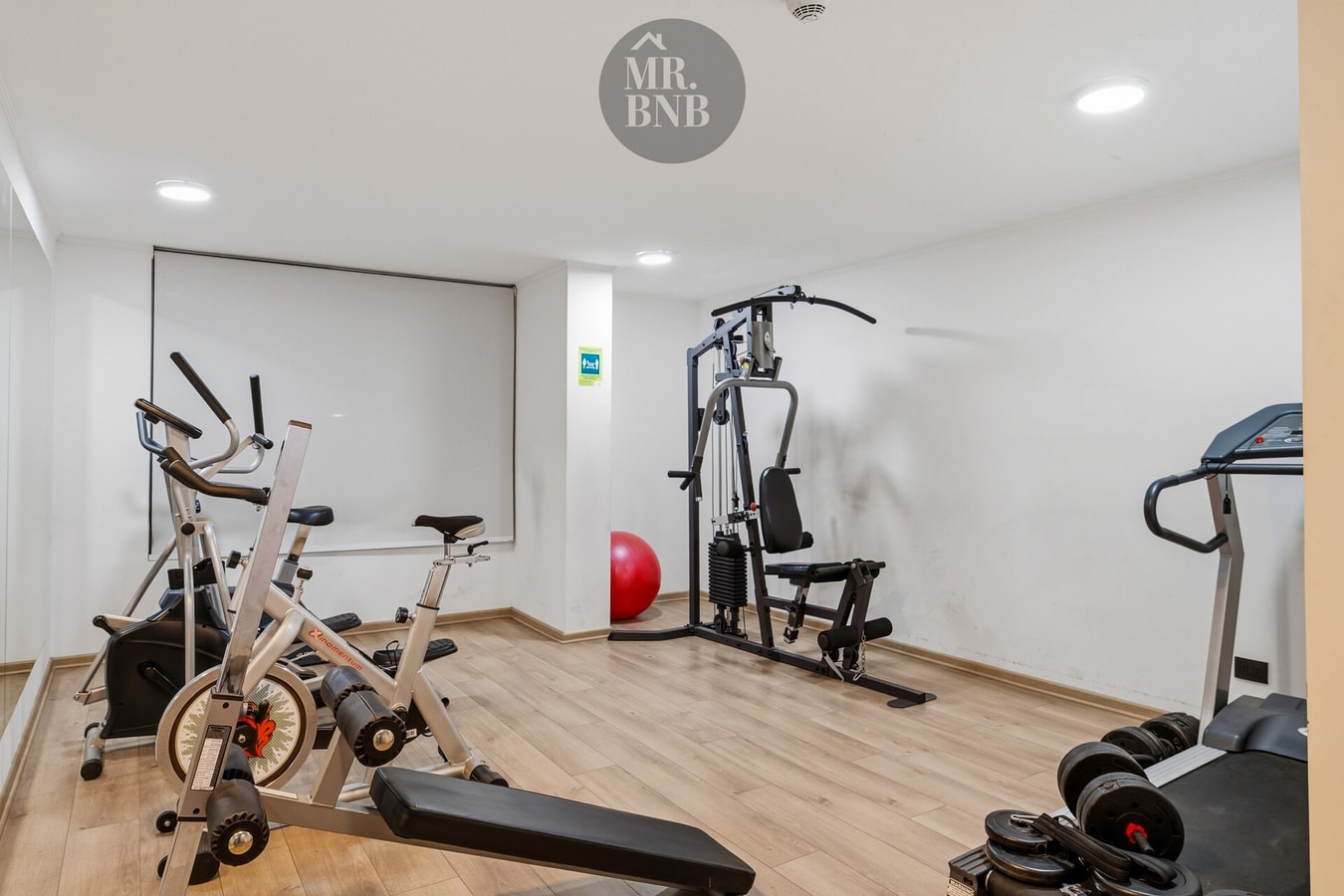 Sala de gimnasio del edificio con bicicletas estáticas, multiestación, balón y trotadora