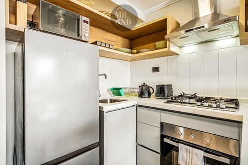 Cocina con refrigerador, microondas, cocina a gas y horno bajo mueble de madera.