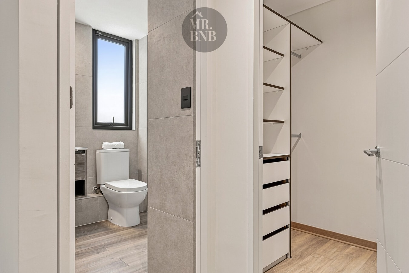 Baño con inodoro junto a walk-in closet con repisas y cajones abiertos