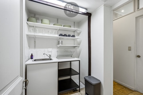 Kitchenette con repisas abiertas, lavaplatos y mesón de trabajo.
