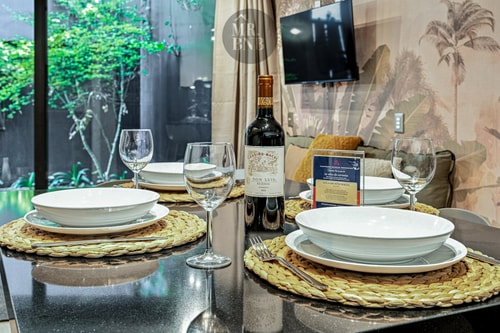 Mesa comedor puesta con platos, copas de vino y botella, sobre papel mural de hojas
