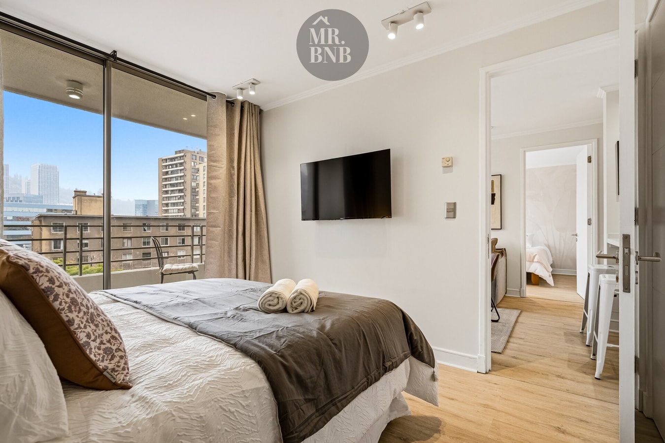 Dormitorio con cama matrimonial, TV montada en la pared y puerta hacia el pasillo