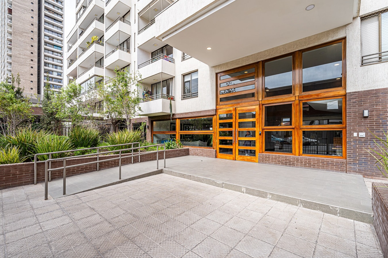 Fachada del edificio con jardín, rampa de acceso y ventanales de madera