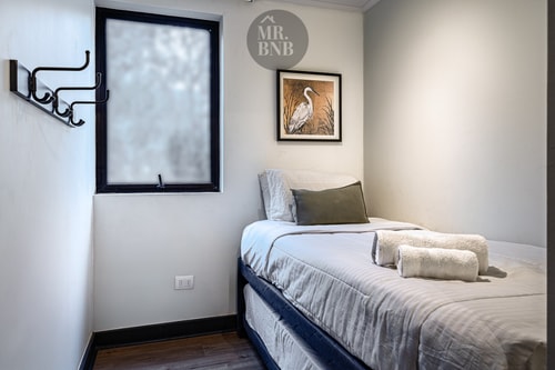 Dormitorio secundario con cama individual, ventana pequeña y cuadro con un ave